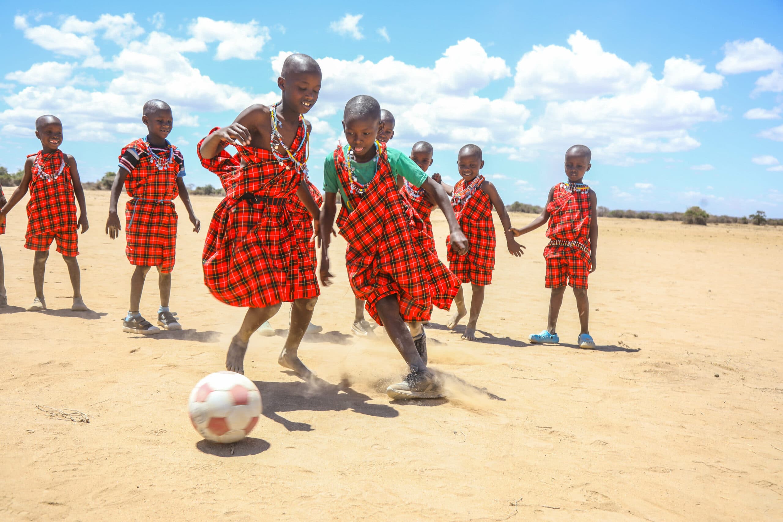 Children playing football outdoors on a sandy field