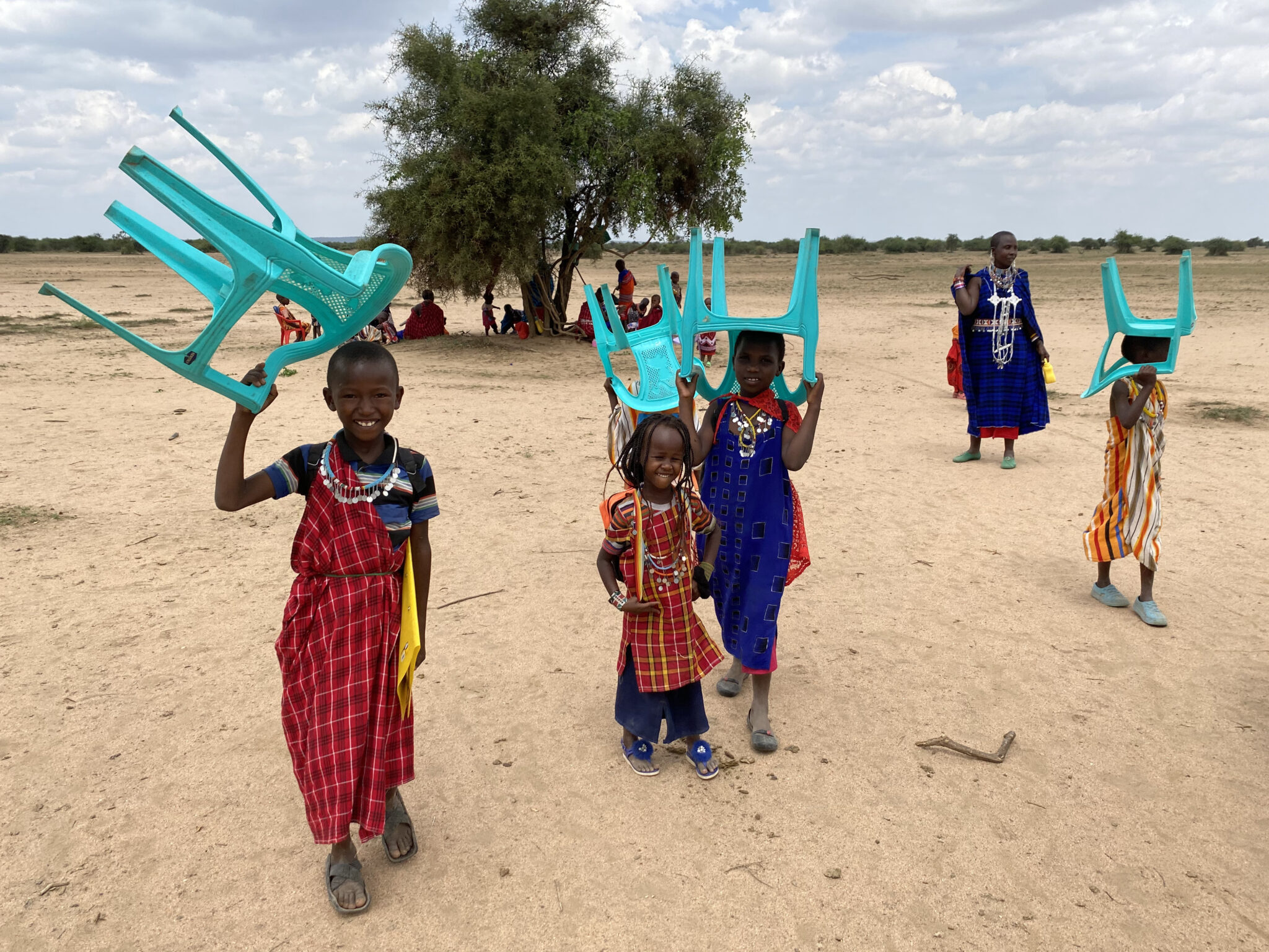 Children carrying turquoise chairs outdoors